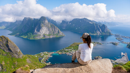 Wall Mural - A lone traveler enjoys the breathtaking view from a mountaintop overlooking the turquoise waters and rugged landscapes of the Lofoten Islands in Norway. Reinebringen, Lofoten, Norway