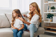© SHOTPRIME STUDIO - Mother and daughter bonding time as mom gently combs her child's hair on a cozy living room couch