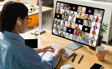 Poster - A woman wearing earbuds sits at her desk in front of a computer monitor displaying a video conference call with many participants. She is actively participating in the meeting