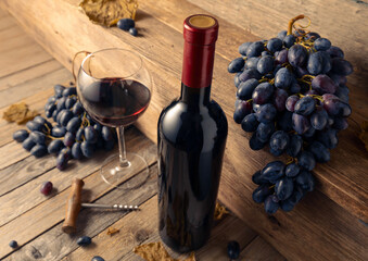 Wall Mural - Bottle and glass of red wine with blue grapes on a wooden table.