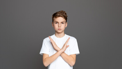 Teenager with arms crossed in an X shape, showcasing refusal or denial, isolated on a grey background