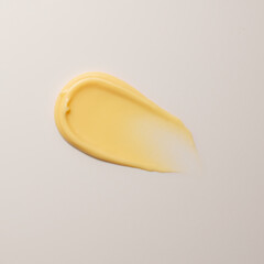 Single vibrant yellow swatch of creamy cosmetic product applied as smear against white background, ideal for color comparison and texture analysis