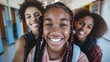 © Z A C - Three young girls smiling at the camera one in the foreground with braided hair another with a backpack and a third with a big smile and curly hair all in a school hallway.