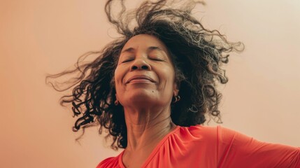 Poster - Woman with curly hair closed eyes and a smile wearing an orange top in a soft-focus warm-toned portrait.