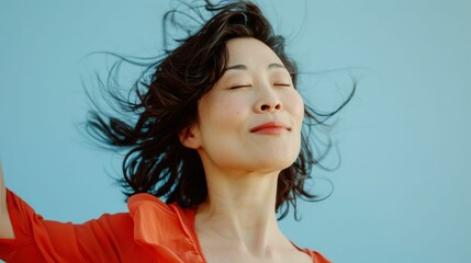 Wall Mural - A woman with closed eyes smiling and with her hair blowing in the wind wearing an orange blouse.