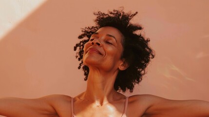 Wall Mural - A woman with curly hair smiling and stretching her arms out with her eyes closed against a warm-toned background.