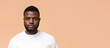 © Prostock-studio - Young Black man with a short haircut and a neatly trimmed beard. He is wearing a white t-shirt and is looking directly at the camera. The background is a solid peach color, copy space