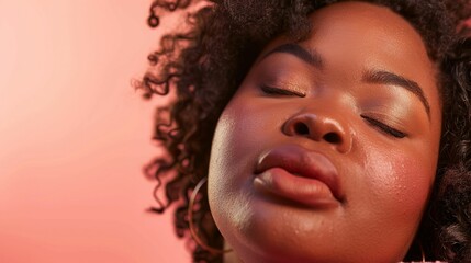 Wall Mural - A close-up of a person with closed eyes full lips and curly hair set against a soft pink background conveying a sense of relaxation or sleep.