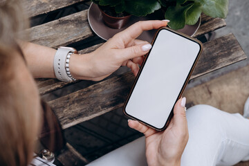 Mockup woman's hand holding using smart phone with white blank screen at coffee shop, mobile app design and advertising, online marketing