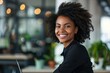 © darshika - Successful Afro businesswoman smiling at laptop in modern office.