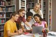 © Prostock-studio - Multinational Team Of College Students Talking Over Project, girl pointing at laptop screen, library interior