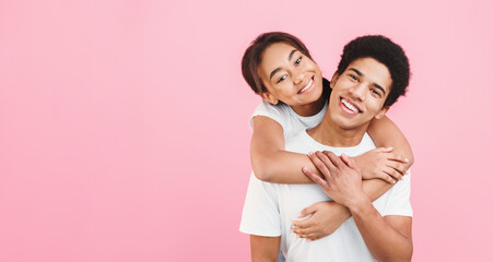 Wall Mural - Man giving piggyback ride to his girlfriend, having fun on pink background