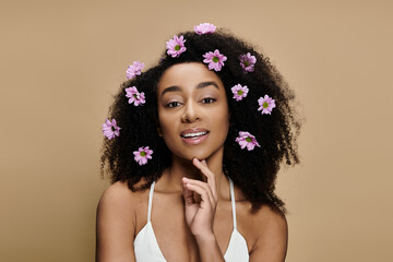 Wall Mural - A beautiful African American woman with natural makeup and flowers in her hair, posing against a beige background.