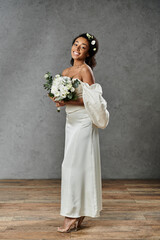 Wall Mural - An African American bride in a white wedding dress and floral crown smiles at the camera, holding a bouquet of white flowers.