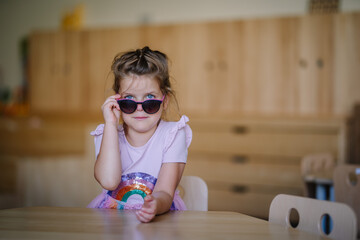 Valmiera, Latvia - September 7, 2023 - A young girl wearing a rainbow dress and sunglasses sits at a table, looking confidently at the camera with a playful expression.