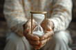 © gearstd - An elderly individual's hands gently cupping a white sand hourglass, symbolizing the passage of time