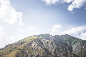 Minimalistic mountain peaks and slopes of rocks with vegetation against the blue summer sky on a sunny summer day in the mountains of Tajikistan in the Pamirs