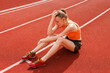 © st.kolesnikov - upset female athletics athlete sitting on a running track in the stadium, losing in a competition