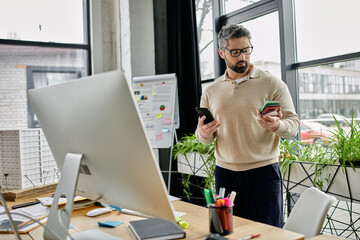 A handsome businessman with a beard stands in a modern office, looking at his phone.