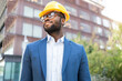 © ADDICTIVE STOCK - Black businessman in hard hat looking away in urban setting