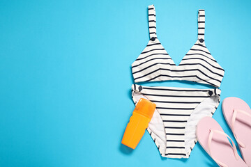 Wall Mural - Striped swimsuit, flip flops and sunscreen on light blue background, flat lay. Space for text