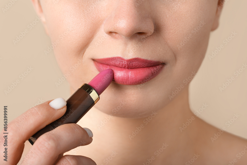 Woman applying pink lipstick on beige background, closeup