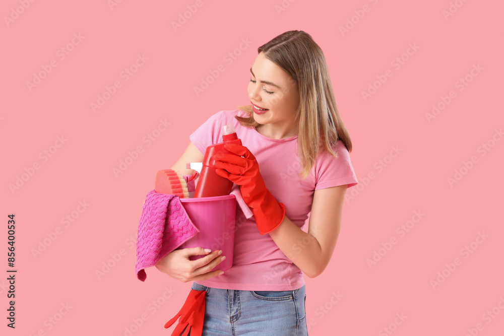 Young woman with cleaning supplies on pink background