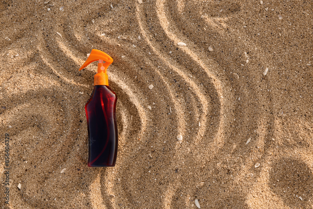 Bottle of sunscreen cream on sand at sea beach