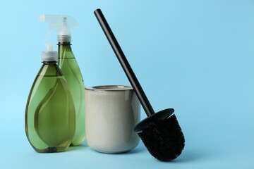 Toilet brush, cleaning products and holder on light blue background