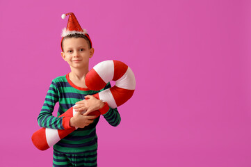 Poster - Cute little boy in Christmas pajamas with candy cane pillow on purple background