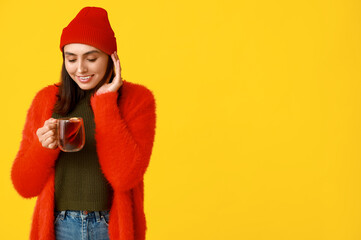 Poster - Happy young woman with glass cup of hot mulled wine on yellow background