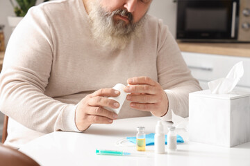 Poster - Portrait of sad senior man sitting at table with tissues and medicine in kitchen