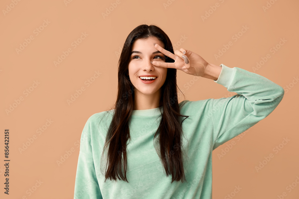 Young woman showing peace sign on beige background