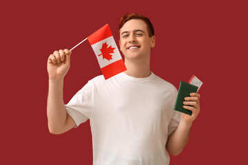 Wall Mural - Handsome young happy man with Canadian flag, passport and ticket on red background