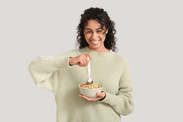 Wall Mural - Smiling young woman holding bowl of tasty cereal rings and spoon on light background