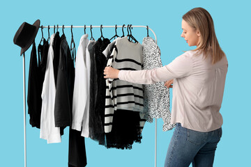 Poster - Happy female stylist with clothes on rack against blue background