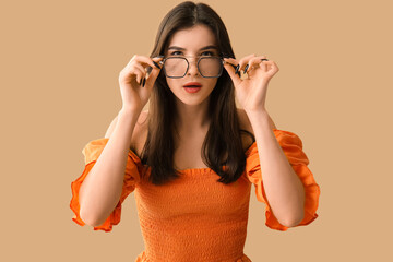 Wall Mural - Beautiful young shocked woman in new eyeglasses on beige background