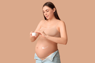 Sticker - Young pregnant woman applying cream against stretch marks on beige background