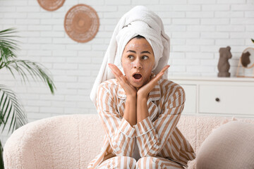 Poster - Surprised young African-American woman in pajamas with facial mask at home