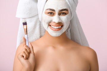 Poster - Happy young African-American woman with facial mask and brush on pink background