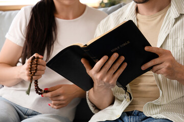 Wall Mural - Religious couple with praying beads reading Holy Bible on sofa at home, closeup