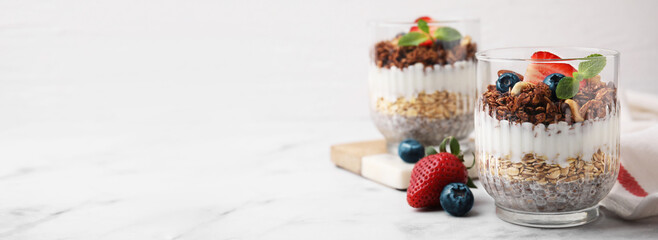 Canvas Print - Tasty dessert with granola, yogurt, chia seeds and berries in glasses on white marble table. Banner design with space for text