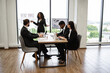 © sofiko14 - Office setting with professional attire, presentation and teamwork. African American business woman standing near window with graphs and charts making report to colleagues.