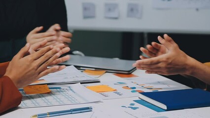 A group of cheerful Asian graphic designers or developers is standing in the meeting, clapping their hands, and celebrating their successful project in the meeting together.