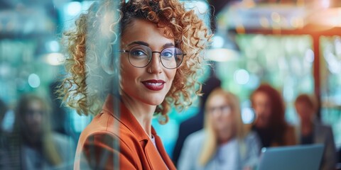 Wall Mural - A woman with curly hair and glasses is smiling at the camera