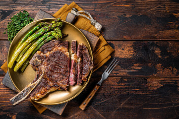 Wall Mural - Sliced Grilled Cowboy or rib eye with bone beef steak, roasted asparagus in a plate. Wooden background. Top view. Copy space