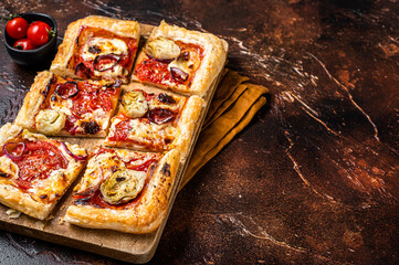 Wall Mural - Vegetarian puff pastry pizza with artichoke, mozzarella, tomatoes and cheese sliced on a wooden board. Dark background. Top view. Copy space