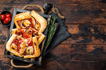 Wall Mural - Puff pastry tart pizza  with artichoke, mozzarella, tomatoes and cheese sliced in a wooden tray. Wooden background. Top view. Copy space