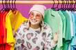 © ViDi Studio - Young lesbian woman wear pink animal clothes show colorful t-shirts wardrobe on rack at store look aside isolated on plain purple background studio portrait. Pride day June month love LGBTQ concept.