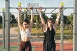 © Jorge - Young couple doing pull-ups at outdoor fitness park. Two fit young adults engage in pull-ups on monkey bars at a sunny outdoor gym